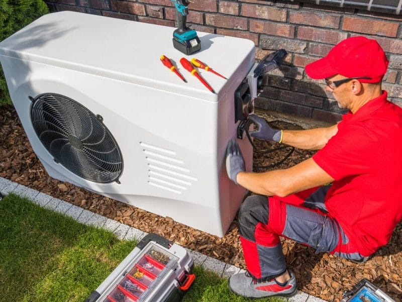 HVAC technician working on an outdoor unit with tools nearby.