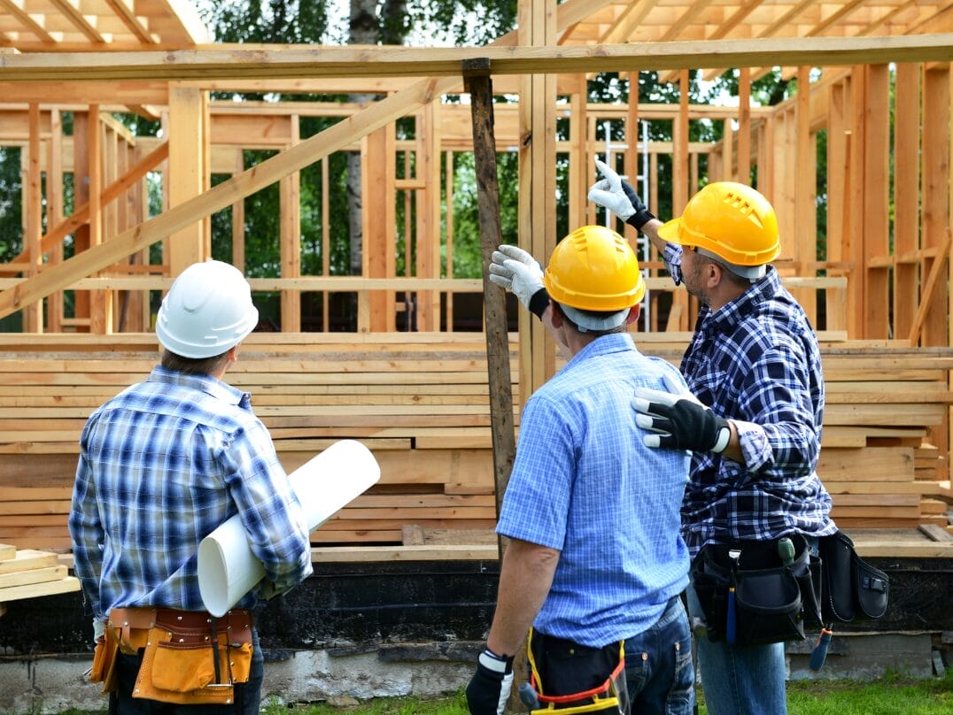 A group of construction professionals in safety gear inspecting the framing of a newly built home.