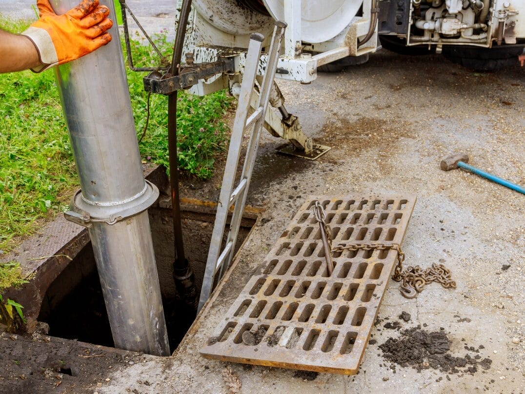 Sewer maintenance worker inserting a large metal pipe into an open manhole during a sewer line inspection.
