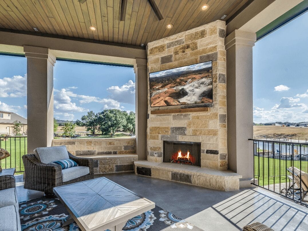 Covered outdoor patio with fireplace, mounted TV, and seating area overlooking a backyard